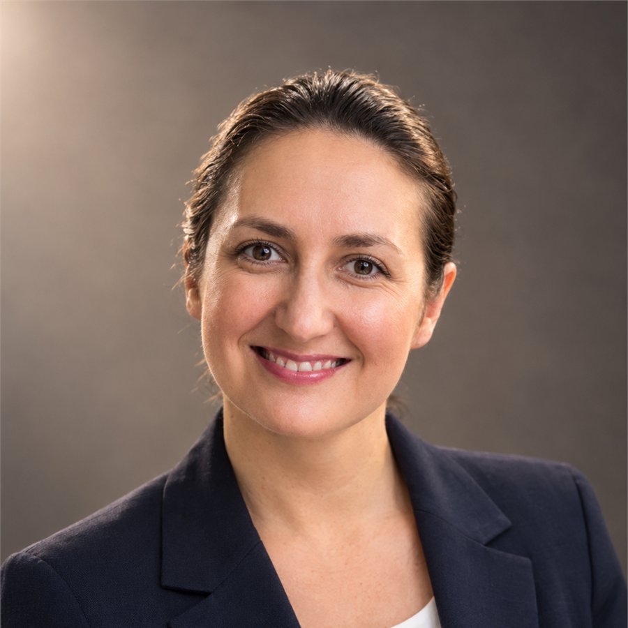 Yana Rulinsky in a navy blazer over a white top, smiling, in a professional studio headshot against a plain grey background.